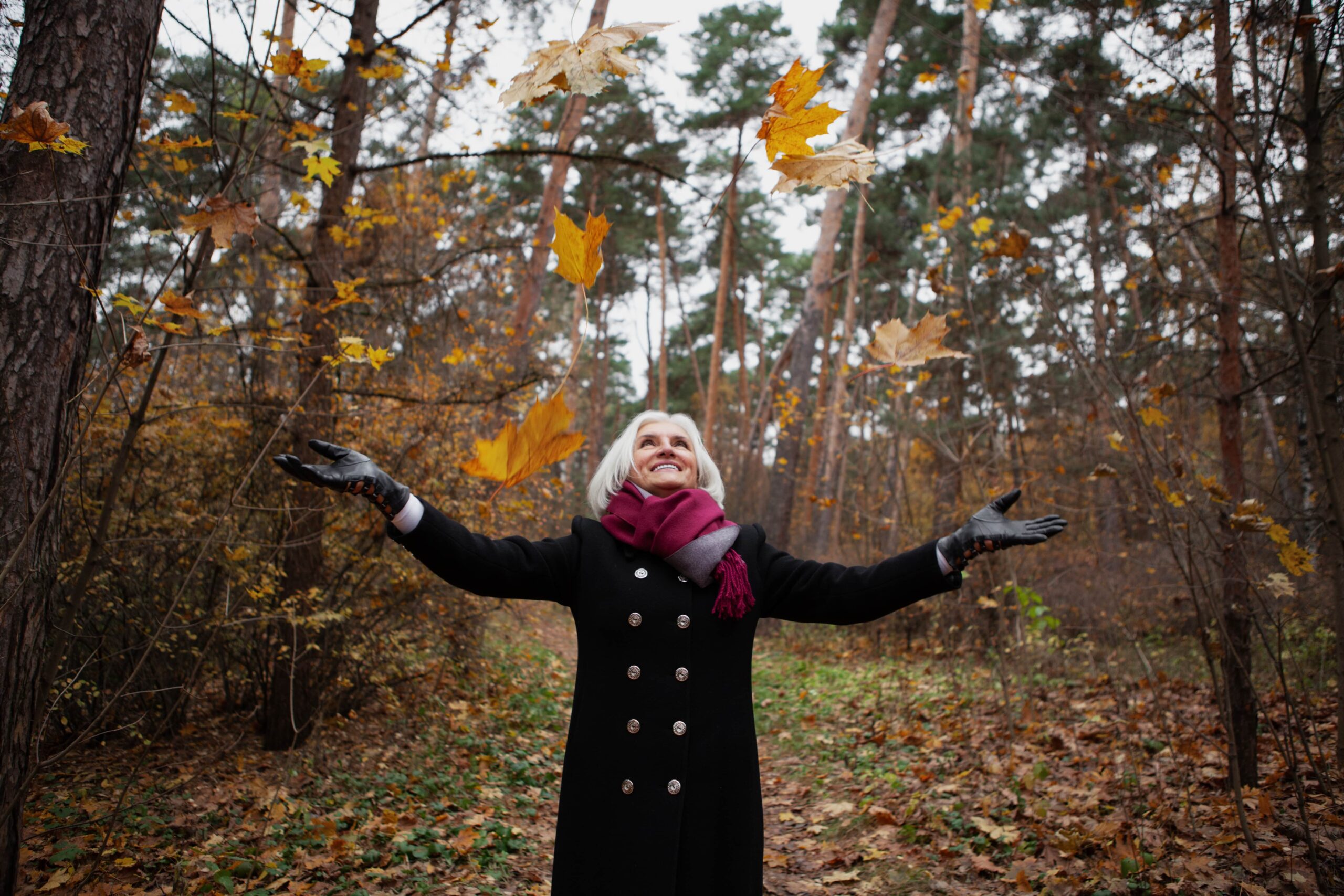 happy-senior-woman-throws-leaves-in-forest-or-natu-2023-11-27-04-56-43-utc-min