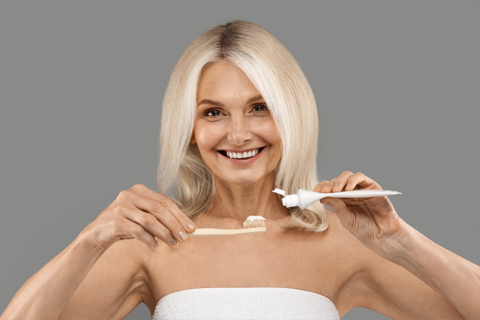 Daily Dental Care. Beautiful Mature Woman Pouring Toothpaste On Toothbrush